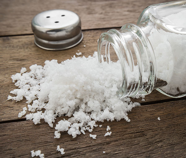 a salt shaker lying on its side, with some salt spilled out onto wooden surface